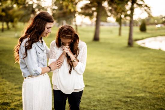 Two young women pray together in an open field.