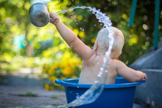 Baby bathing and throwing water in a cup A baby in a small tub uses a cup to throw water.
