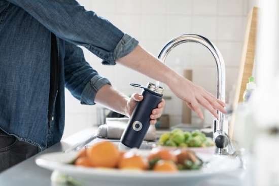 Filling a water bottle with water Woman filling up a water bottle at her kitchen sink.