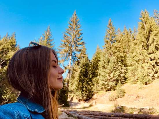 A woman breathing in fresh air as she stands next to a forest.