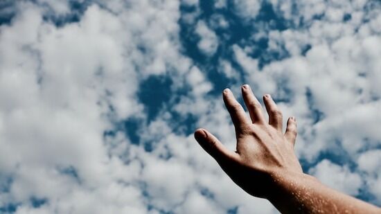 Hand to Sky Man's hand stretched towards the cloudy blue sky as we recognize in the Lord's prayer that God is highly exalted