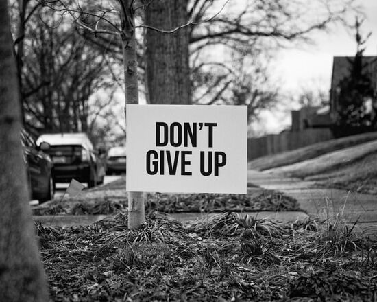 Sign on the lawn that says Don't Give Up A sign near a sidewalk reading, 'Don't Give Up.'