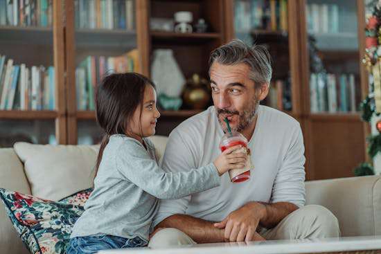 Girl Giving Healthy Drink to Father A smiling young girl holds a smoothie cup out to her father as he tastes it.
