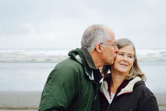 Healthy older couple on beach An older man kissing the cheek of his wife as they enjoy good health and time on the beach together