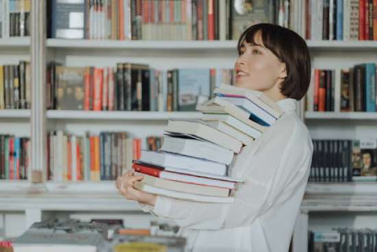 Woman carrying a stack of books in a bookstore Woman carrying a stack of books in a bookstore
