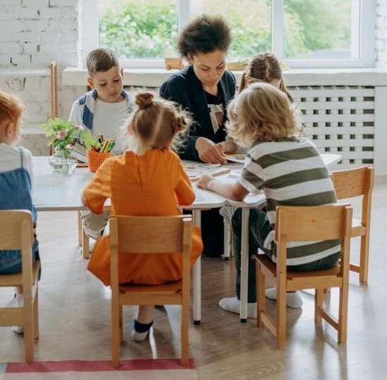 Teacher Kids Sabbath School A woman sitting at a table with children and instructing them during sabbath school