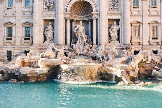 The Trevi Fountain in Rome, Italy, depicts water flowing from several greek figures carved out of stone on the side of a building.