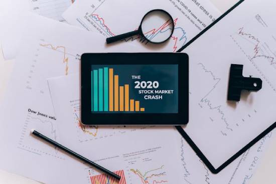 Analytics papers surrounding a tablet that reads "The 2020 Stock Market Crash" A tablet with graphs on a desk, illustrating stock market analytics, which often comes to mind during times of economic insecurity.