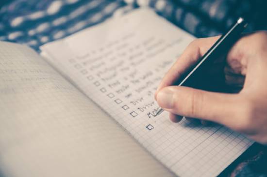 Someone Writing a Checklist in a Notebook Someone checking off a checklist with a pen demonstrates that legalists tend to treat God's law as a checklist for salvation.