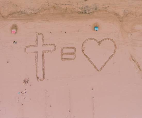 Overhead view of sand art with a message of the cross equals love An overview of a cross, equal sign, and heart drawn on the sand, illustrating how the message of the cross is love.
