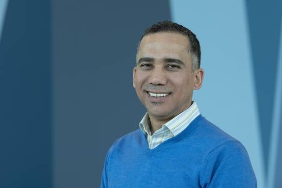 A man in a blue sweater greeting with a smile. He's just one of many examples of laypeople in the church.