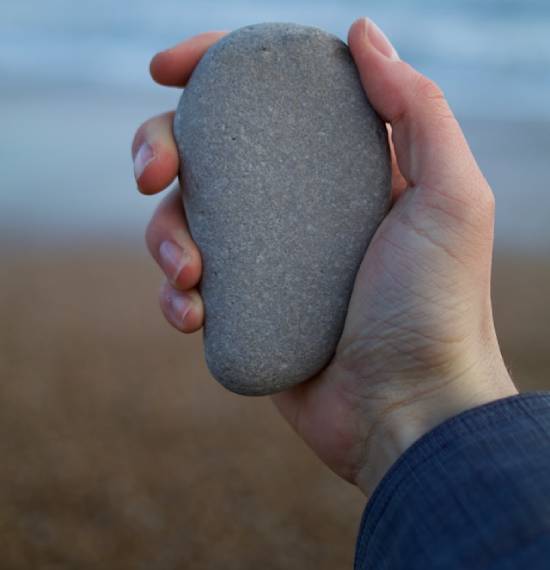 Someone's hand holding a large, smooth, grey stone A person holds up a large, smooth stone in their hand