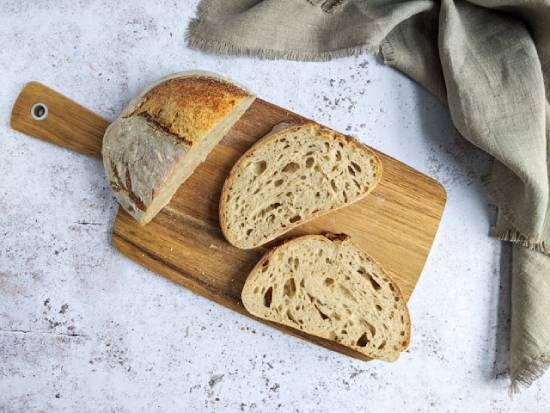 A loaf of bread partially sliced on a wooden cutting board A fresh loaf of bread has a couple of slices cut off from it on a cutting board, symbolizing Jesus as spiritual nourishment.