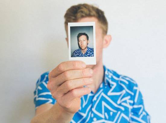 Man holding a picture of himself in front of his face young man holds a headshot of himself in front of his own face.