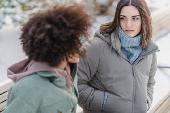 Two women having a serious discussion outdoors on a cold day Two young women are in deep discussion, representing resolving a sensitive conflict within their friendship.