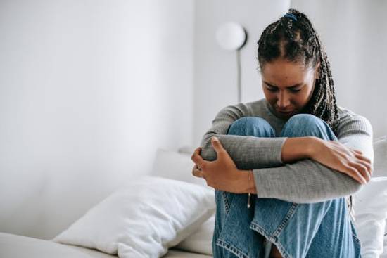 Woman embracing her knees feeling regret for her sins A distressed young woman hugs her knees to her chest