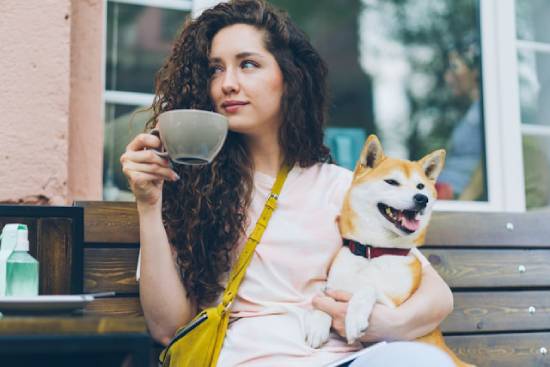 Woman on a bench with her dog and a mug thinking about being a child of God A woman drinks coffee on a neighborhood bench, her dog in her lap.