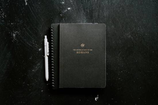The Book of Romans lays on top of a notebook next to a pen to encourage the study of Romans.