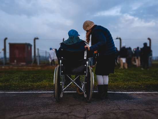 Modest woman helping someone in wheelchair A woman focused on helping someone in a wheelchair in need
