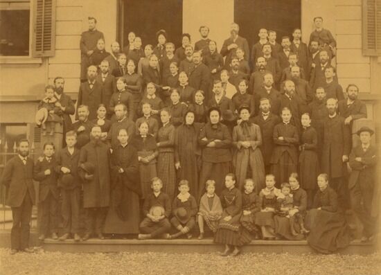 Ellen G white at the Swiss conference Meeting, Sept 1885. A sepia photo of Ellen G. White and many others at a conference in Basel, Switzerland. The image features several rows of people and includes a group of children sitting in the front.