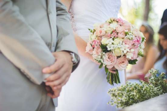 Man and Woman Marriage Bride and groom stand by one another at the altar, the bride holding a bouquet of pink and white roses.
