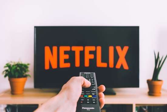 Person Holding Remote Control Entertainment A hand pointing a T.V. remote at a T.V. screen to pull up the latest Netflix shows.