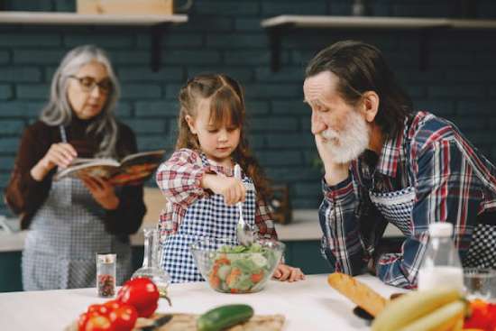 A young girl making a salad with her grandparents