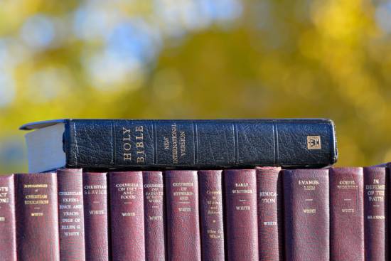 A collection of Ellen White's books with the Bible stacked on top of them