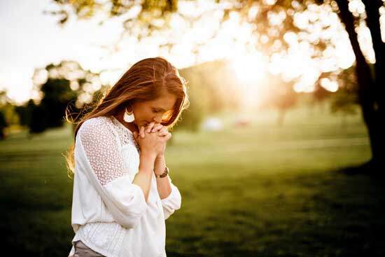 Woman Praying A woman bowing her head in prayer and clasping her hands as she prays to God for salvation