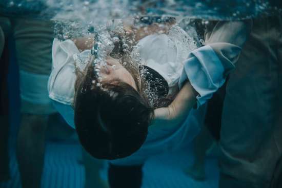 Young woman immersed under the water in baptism A young woman in a white robe is submerged underwater by a hand, signifying baptism's idea of death and burial.