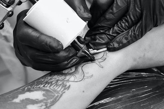 A tattoo artist creating a tattoo on a man's arm.