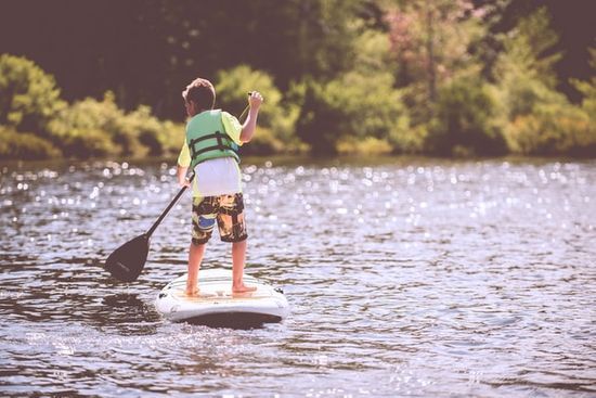Child Paddling at Camp A child riding a paddle board on a lake at summer camp
