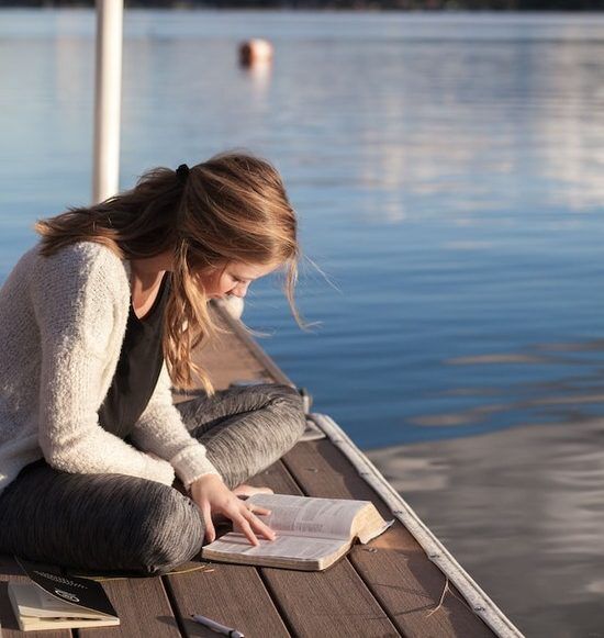 Bible Study A girl sitting on a dock and reading the Bible to discover God's love