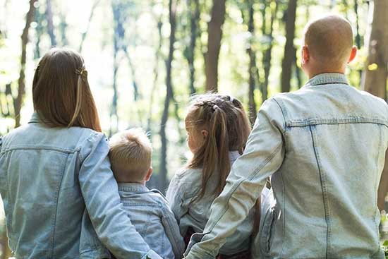 Two parents and their children with arms around one another out in nature Family sitting outdoors with father and mother holding hands