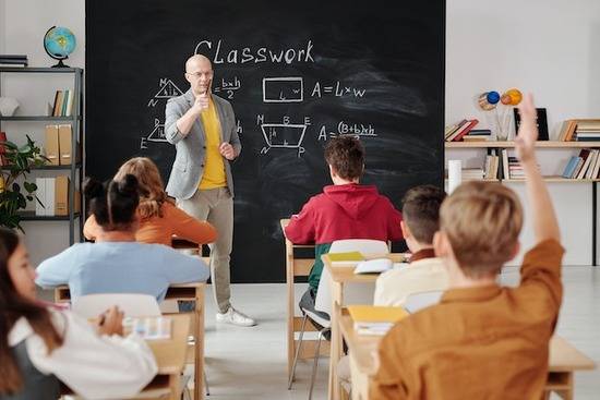 A teacher at the front of a class of students A teacher calling on a student who has his hand raised during math class.