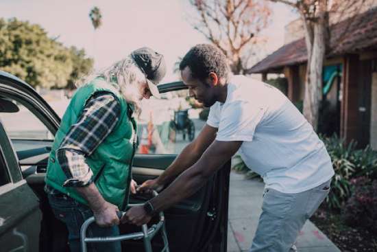 Young man helping elderly man A young man helping an elderly man get out of the car and use his walker