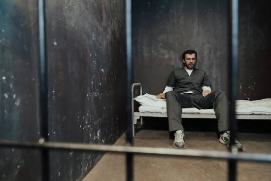 Man Sitting on a Bed in a Jail Cell A man sitting on his cot behind bars in a jail cell demonstrates that lawlessness is just as dangerous to our souls as legalism, according to the Bible.