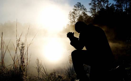  A man kneeling in prayer beside a foggy lake.